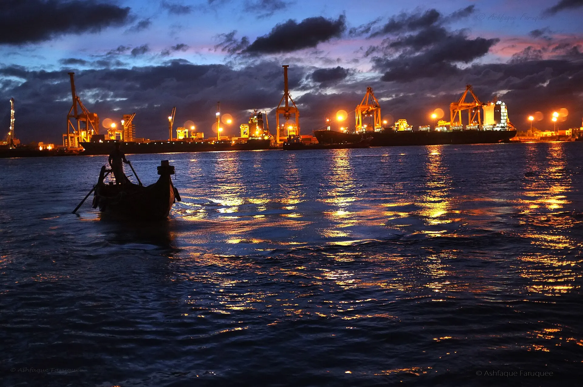 A boatman on the Karnaphuli River at night with the lights of the port behind